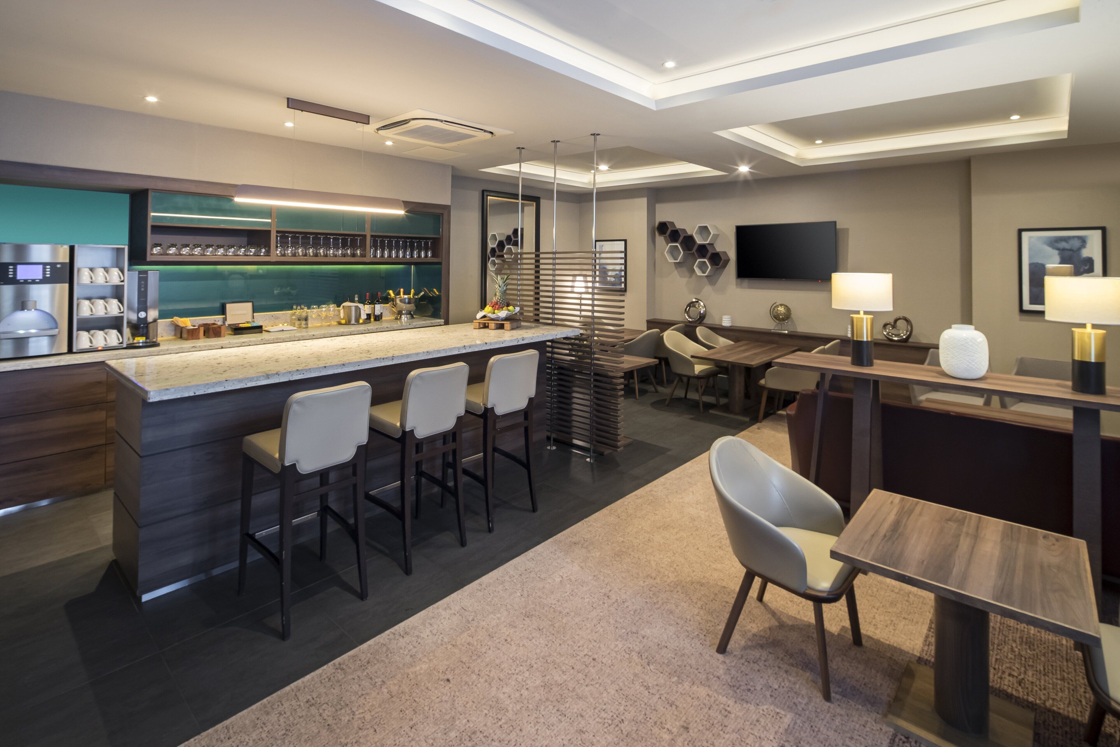 A modern kitchen with a bar area, bar stools, a dining table with chairs, and a flat-screen TV mounted on the wall.