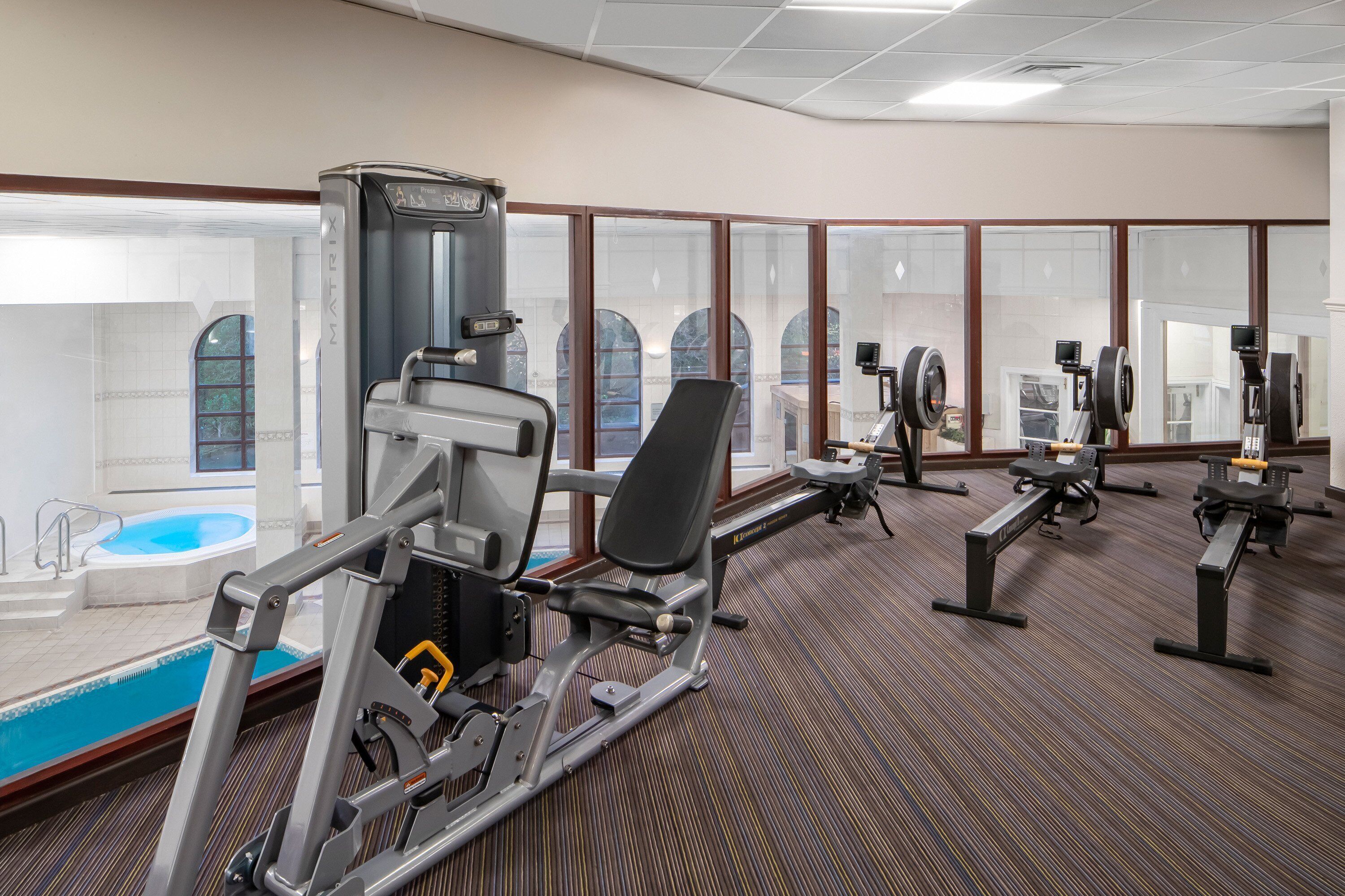A gym with various exercise machines, a pool, and large windows.