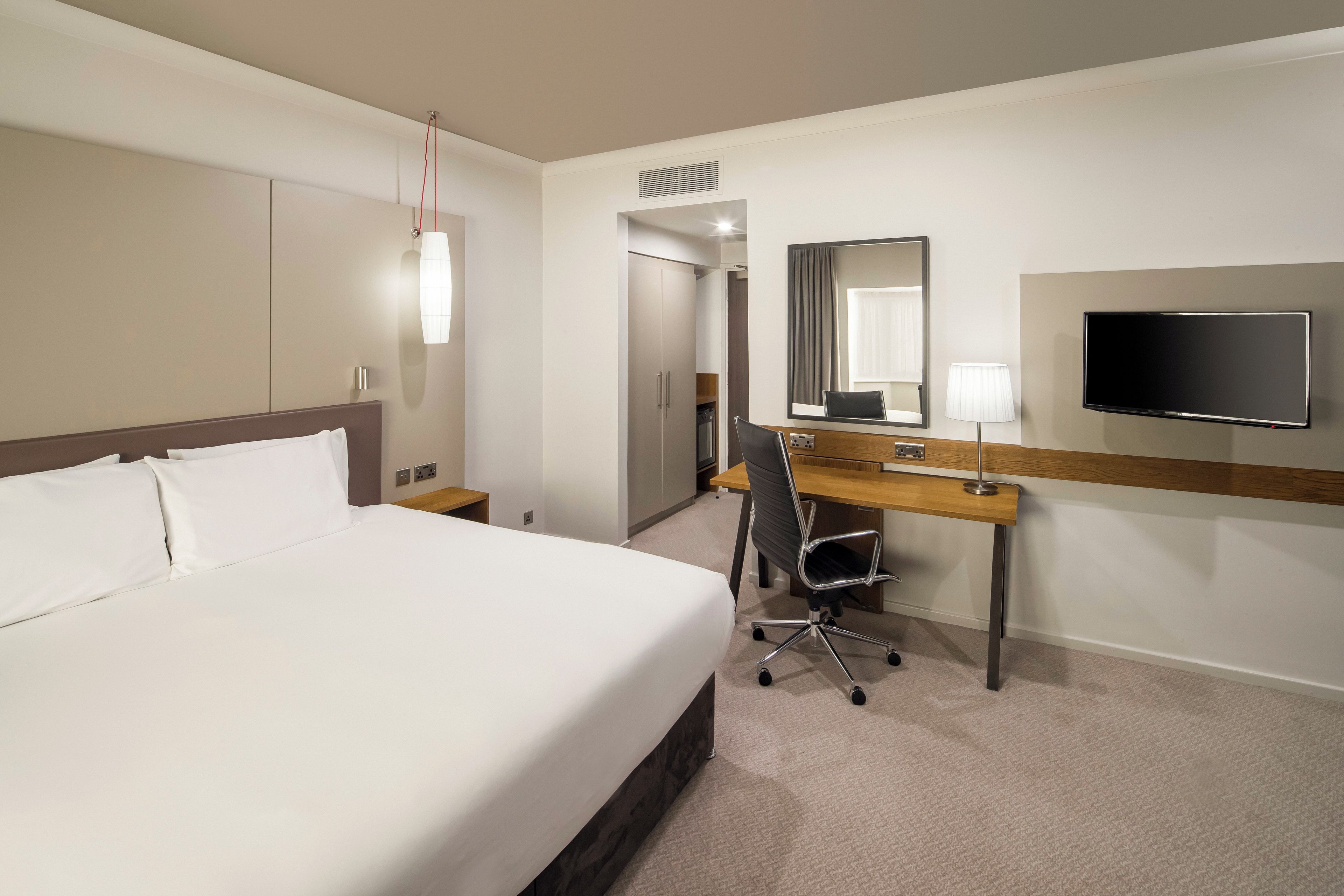 Een hotelkamer met een groot bed, een bureau met stoel, een televisie en een spiegel.