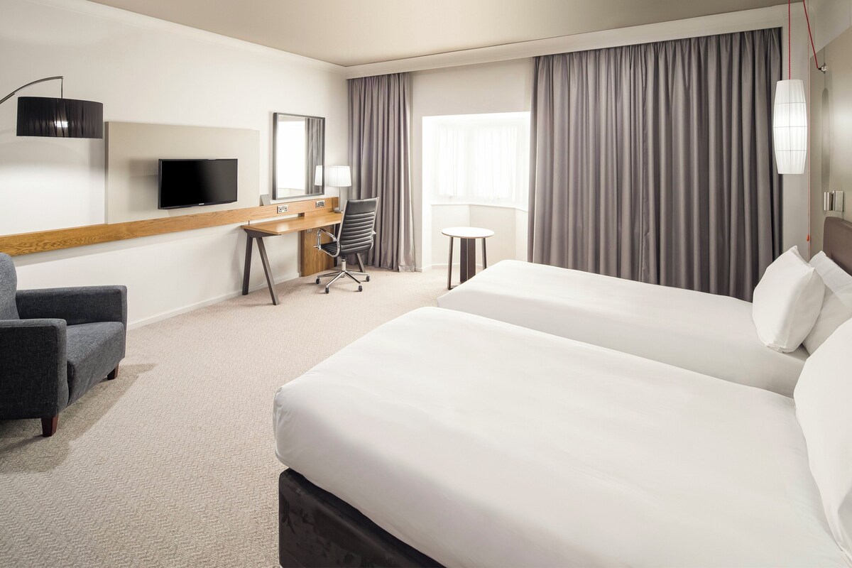 A hotel room with a large bed, a desk with a chair, a television, and a small table.