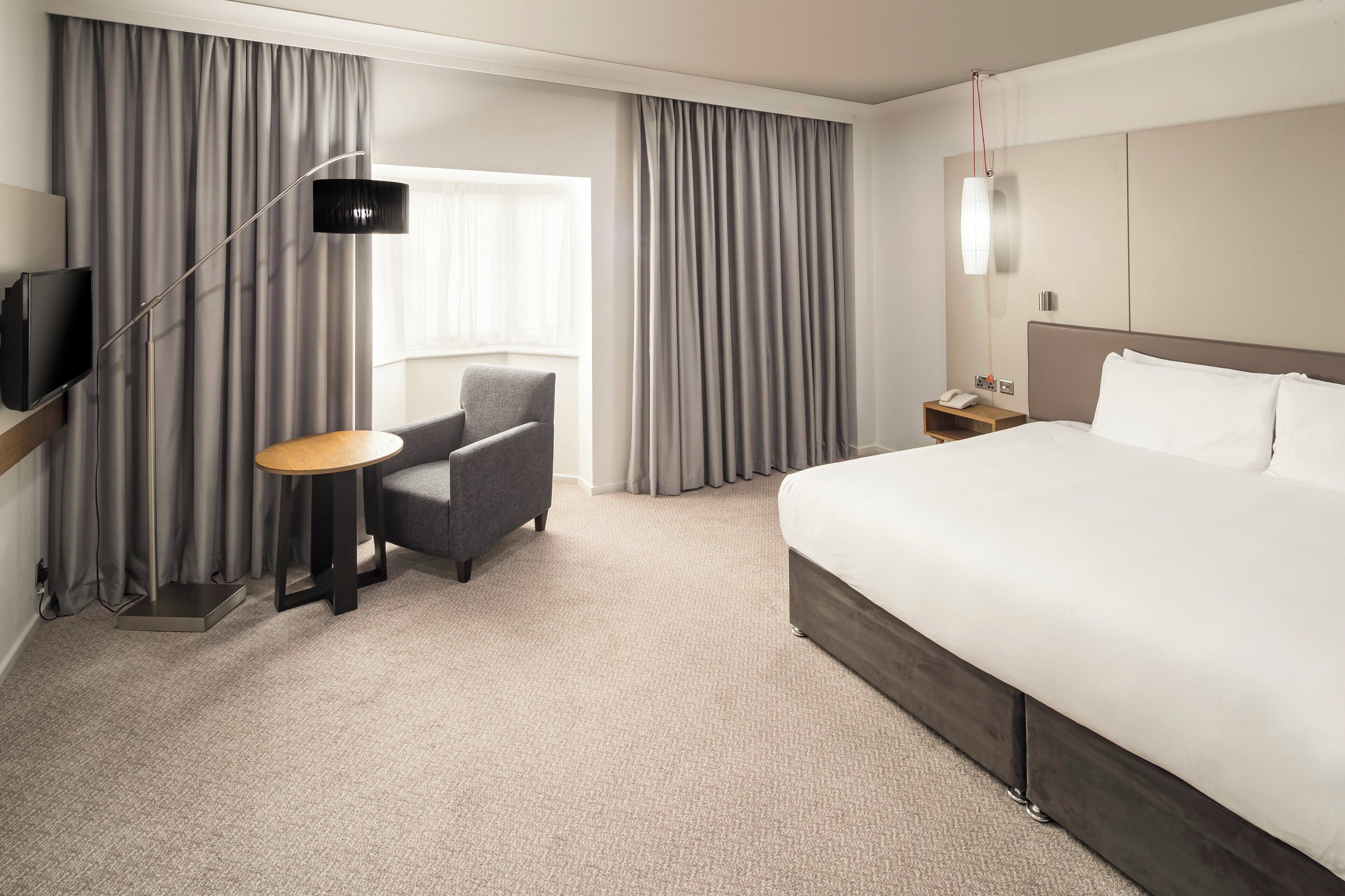 A hotel room with a large bed, a desk with a chair, a TV, and curtains.