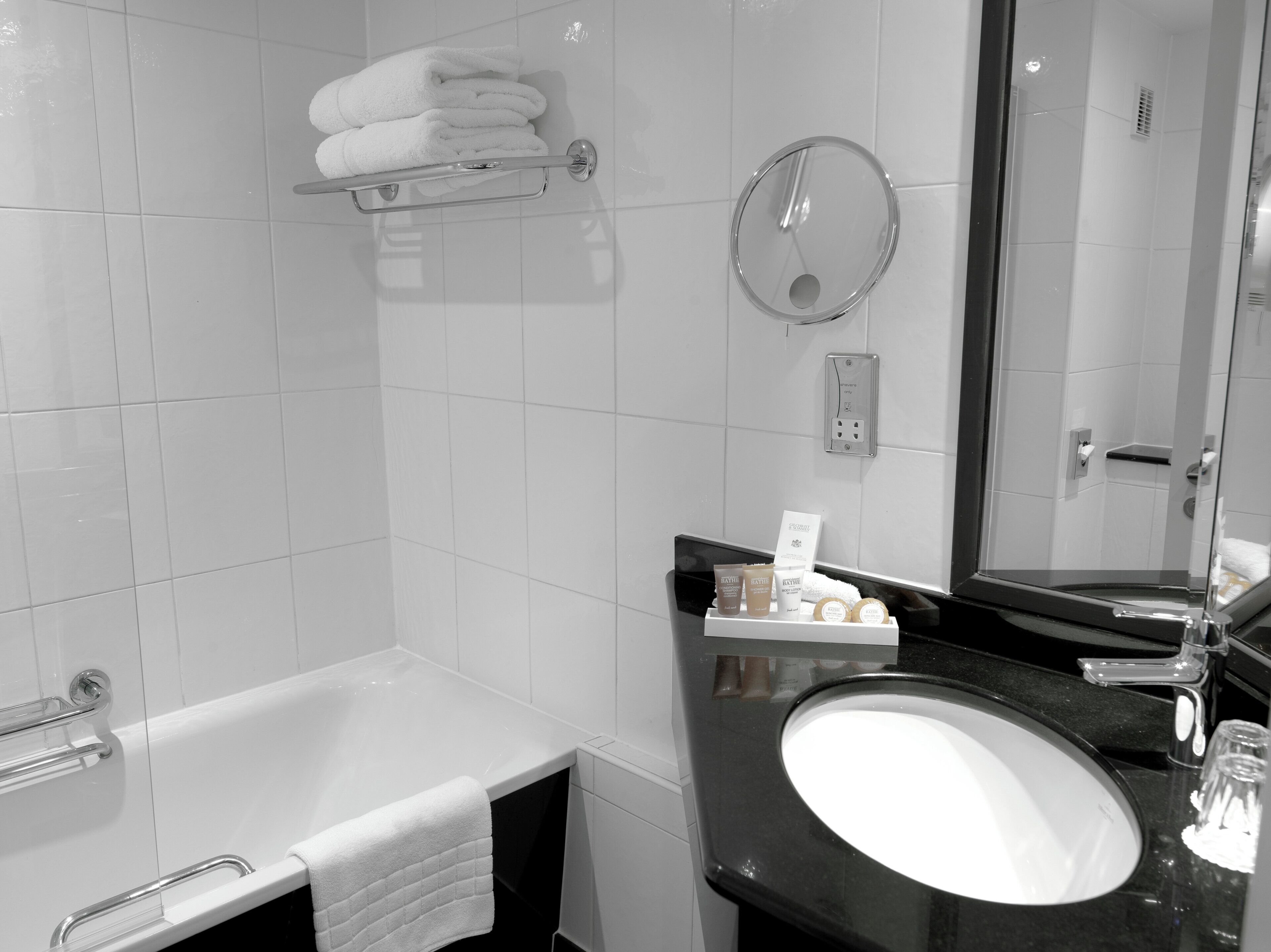 A modern bathroom with a white bathtub, a black sink, and a mirror.