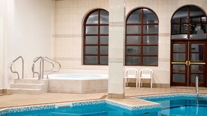 Une piscine intérieure aux murs carrelés, un jacuzzi et deux chaises blanches.