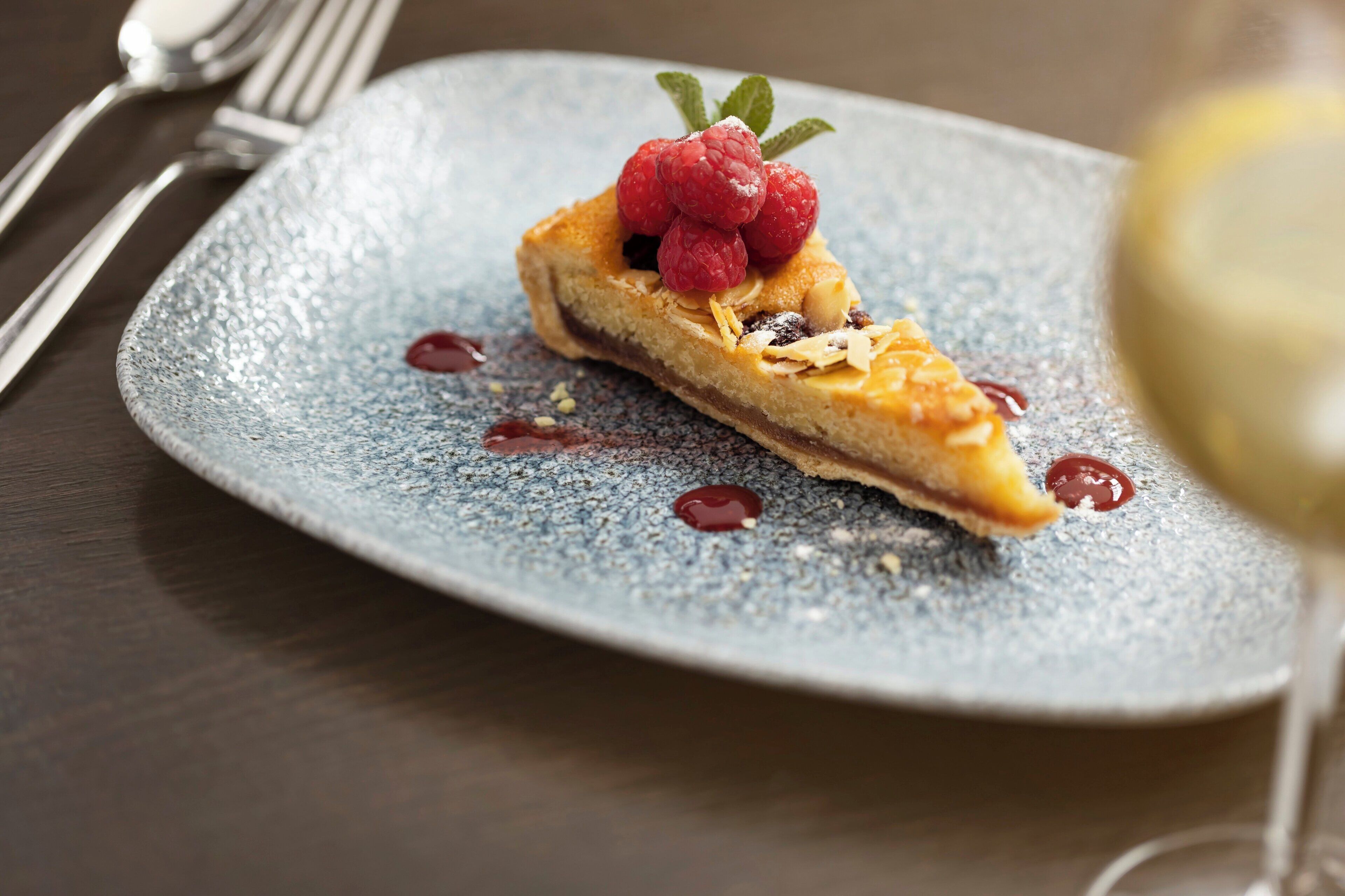 Une part de tarte aux framboises, saupoudrée de sucre glace, présentée sur une assiette à la texture particulière.