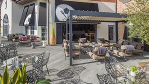 Un espace extérieur aménagé en terrasse, avec différents coins salon comprenant des canapés et des fauteuils, ainsi qu’une table en verre.