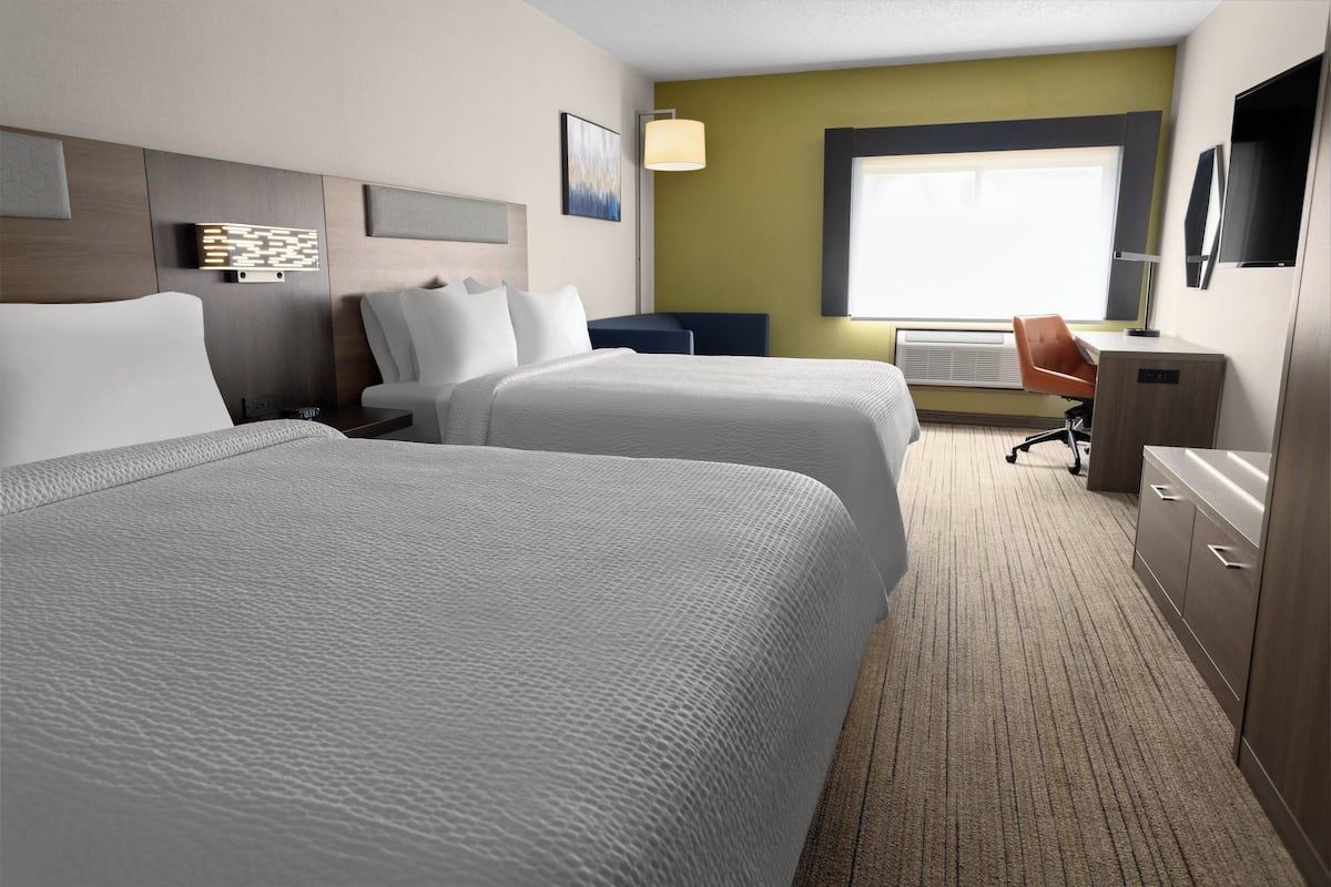 A hotel room with two beds, a desk, a chair, and a TV.
