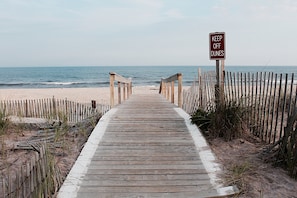 Pasarela de madera que conduce a una playa, con un letrero que dice 'KEEP OFF DUNES'.