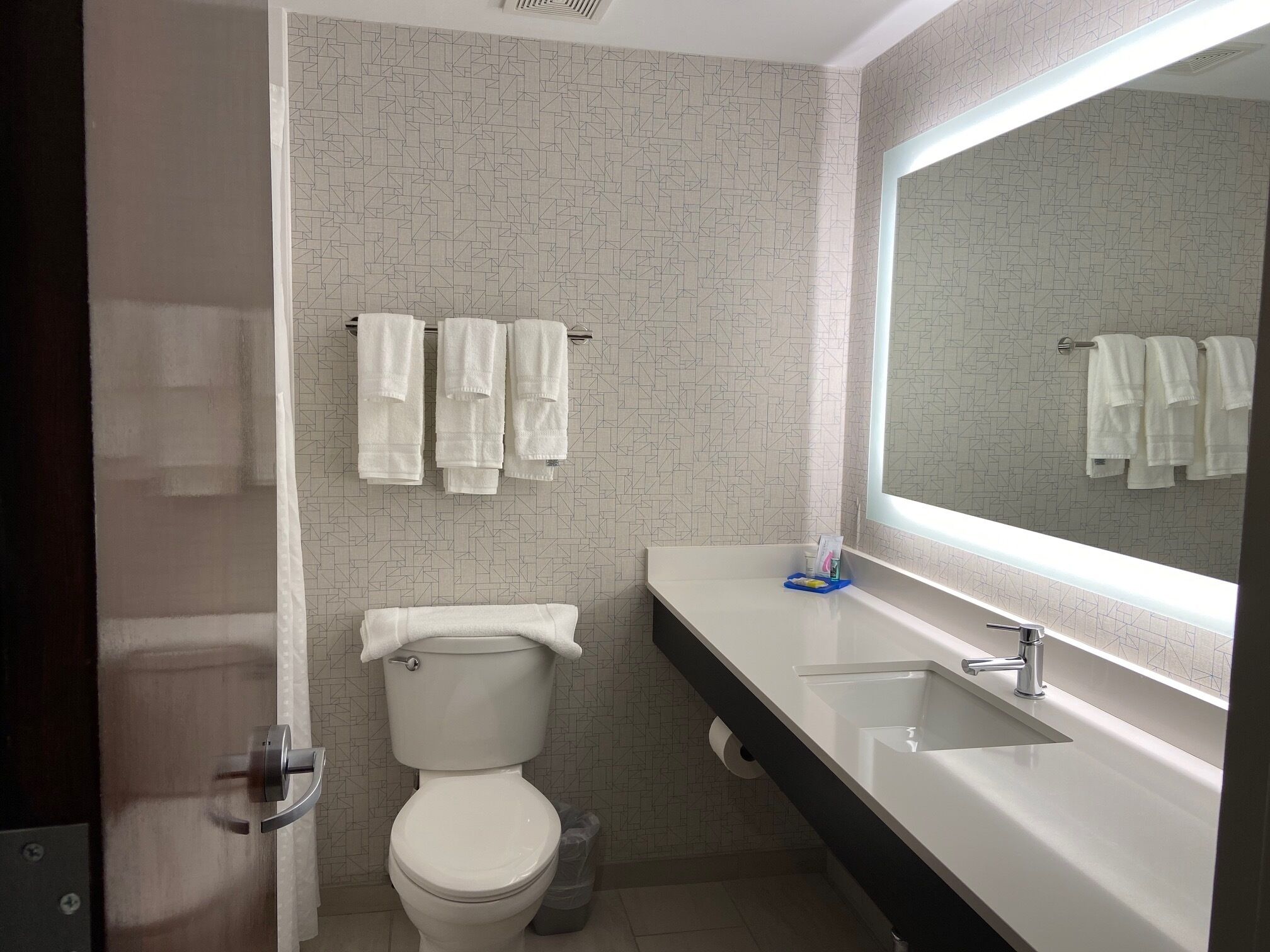 A bathroom with a toilet, a sink, a mirror, and towels hanging on a rack.
