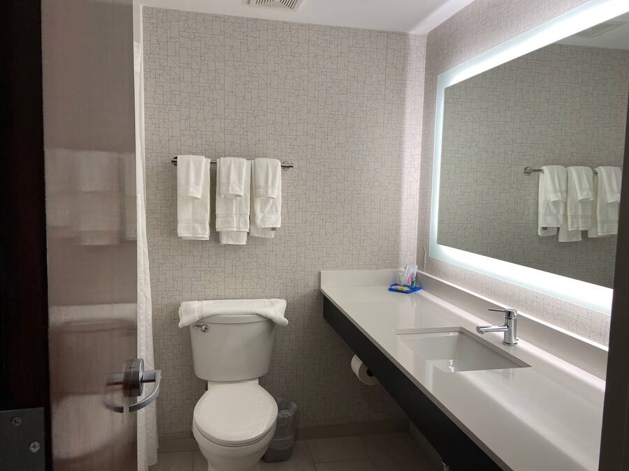 A bathroom with a toilet, a sink, a mirror, and towels hanging on a rack.