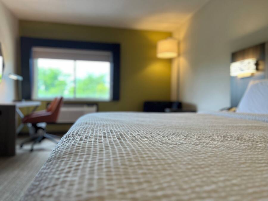 A hotel room with a bed, a desk, a chair, and a window.