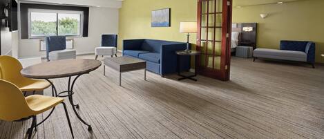Habitación de hotel con sofá, una mesita, una silla, una lámpara y una cama.