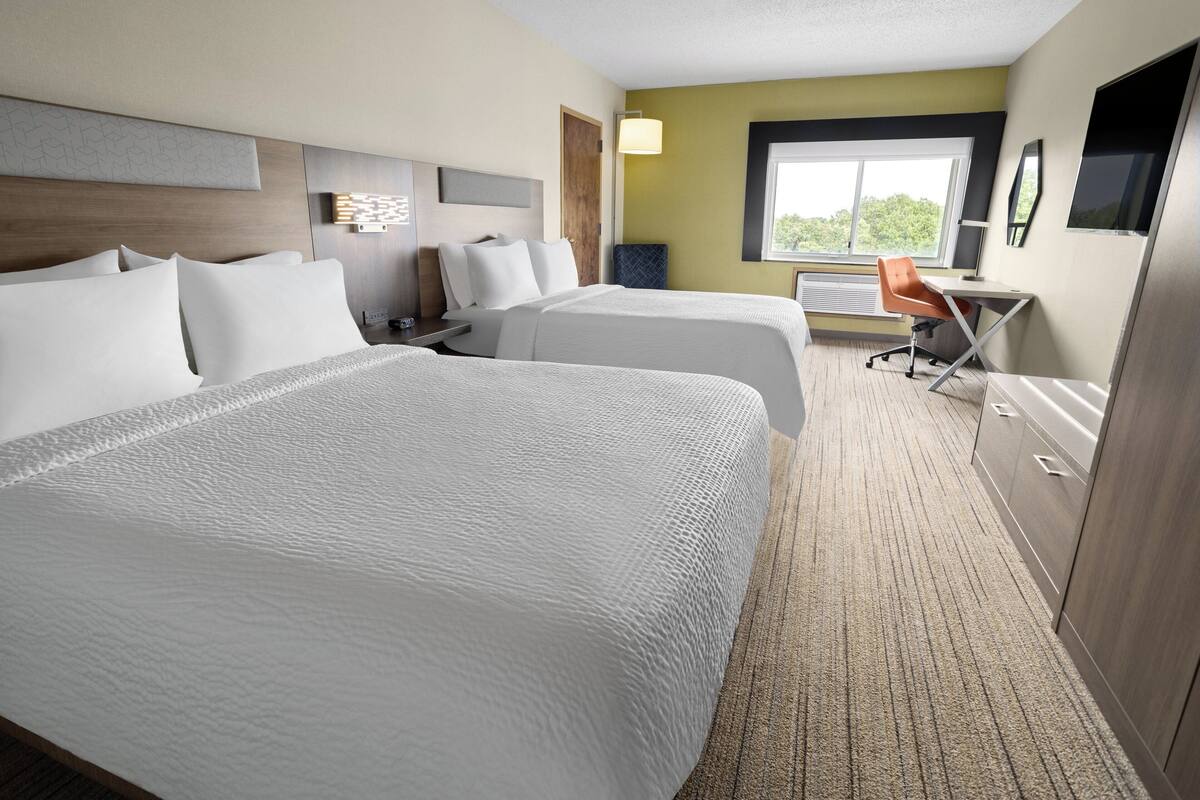 A hotel room with two beds, a desk, and a chair.