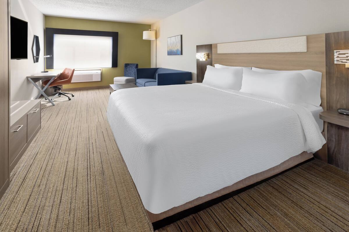 A hotel room with a large bed, a desk with a chair, a sofa, and a TV.