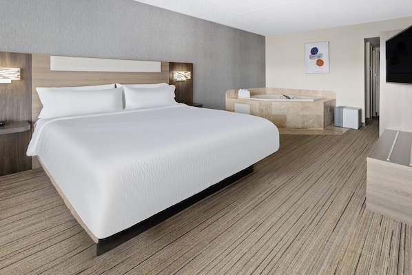 A modern hotel room with a large bed, a wooden headboard, a built-in bathtub, and a flat-screen TV. - Holiday Inn Express Stony Brook by IHG (Centereach)