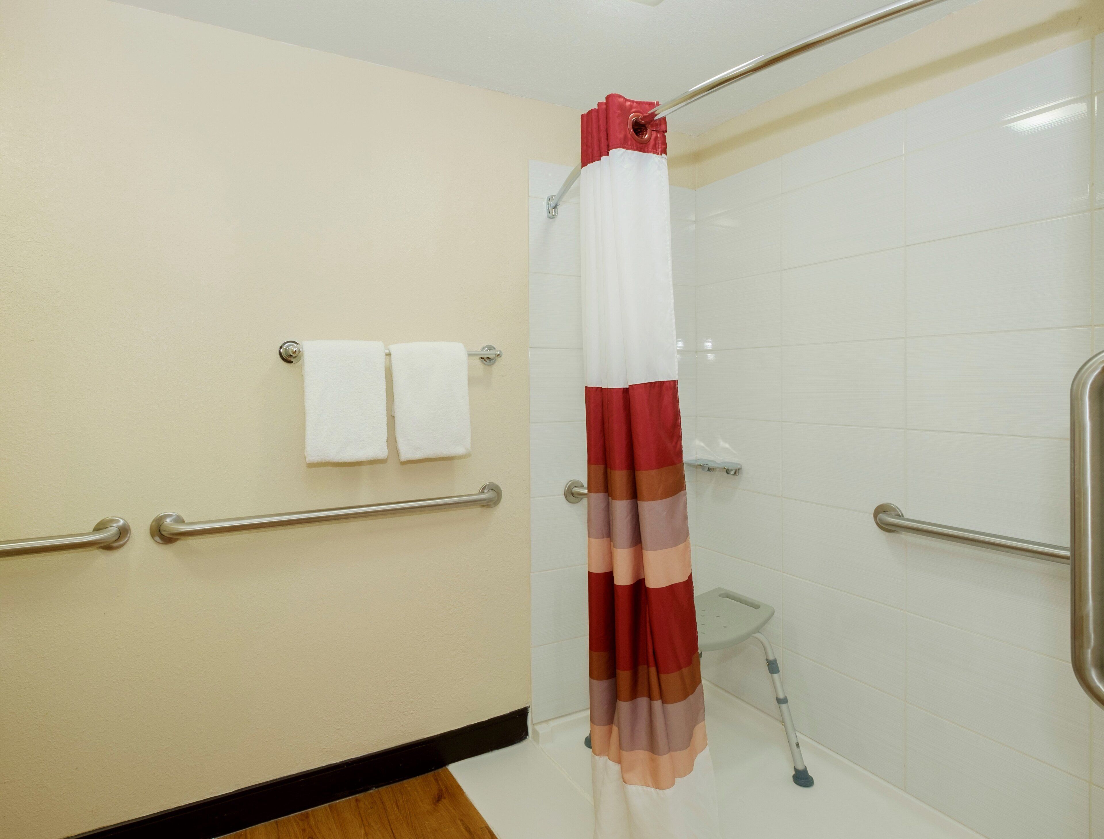 Ein Badezimmer mit Duschvorhang, Haltegriffen und Handtuchhalter.