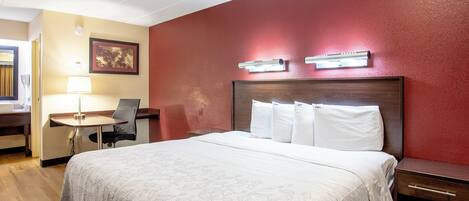 Habitación de hotel con cama, escritorio, silla y lámpara de pared.