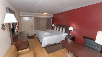Habitación de hotel con cama, mesitas de noche, escritorio, silla y pared decorada en rojo.