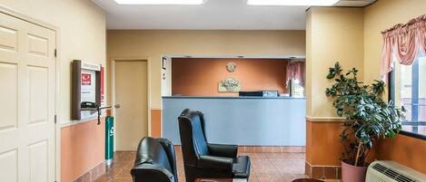 Un hall d’hôtel avec un comptoir d’accueil, deux fauteuils en cuir, une petite table, une plante en pot et un radiateur.