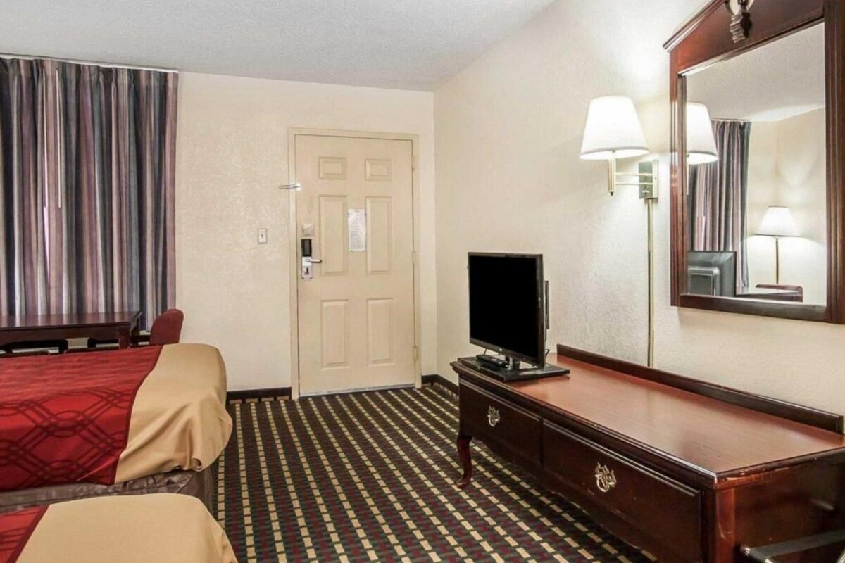 Habitación de hotel con dos camas, televisión, cómoda, espejo y puerta.