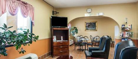 A hotel lobby with a dining area, a TV on a stand, a clock, and a plant.