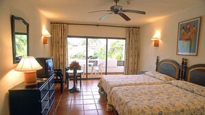 Une chambre d’hôtel avec deux lits, un bureau avec une lampe, un ventilateur de plafond et une vue sur l’extérieur grâce à une porte coulissante.