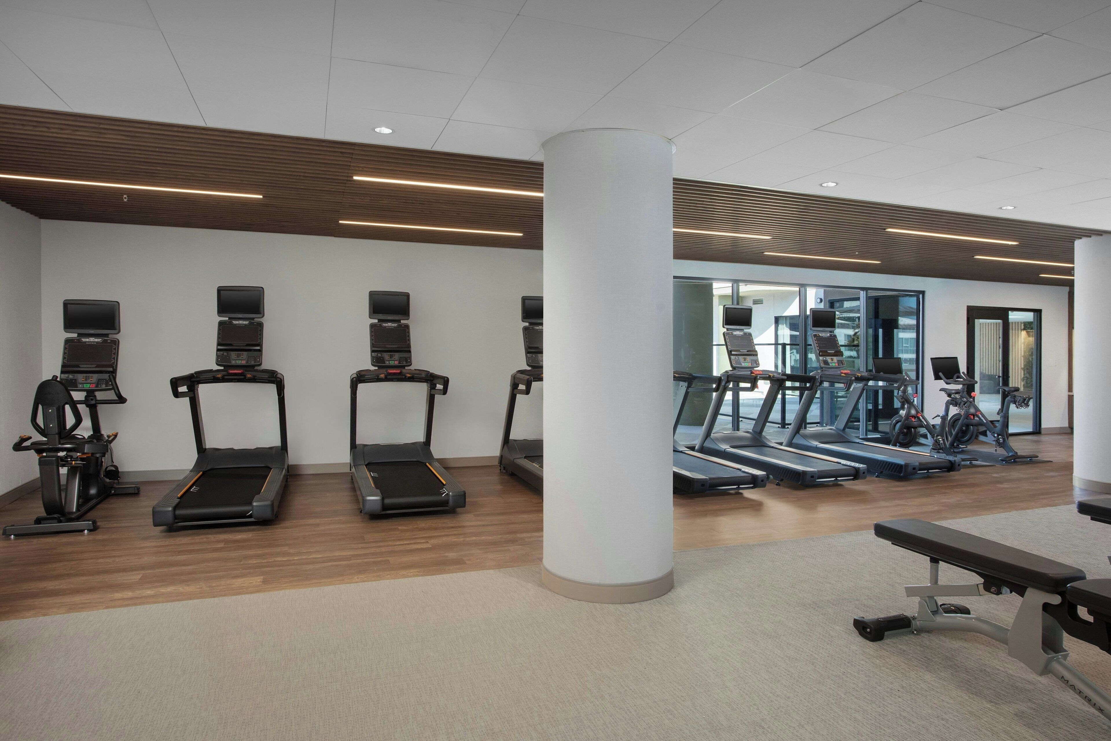 A modern gym with treadmills, elliptical machines, and a bench area.