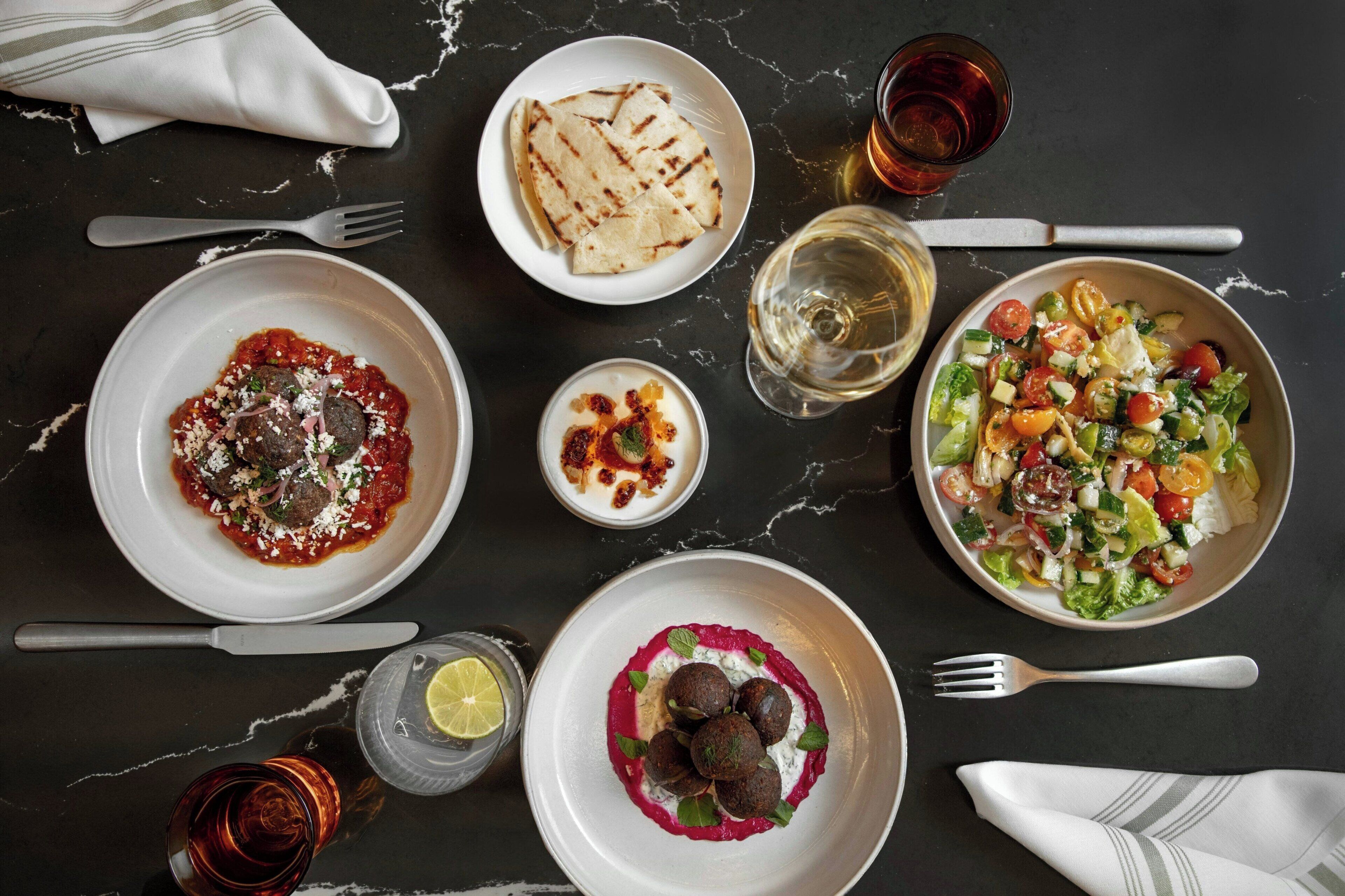 A table set with various dishes including pasta, a salad, and a dessert, with drinks and cutlery.