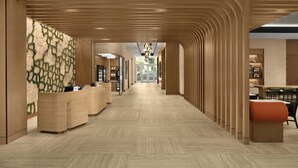 A modern hotel lobby with a wooden reception desk, a patterned wall, and a long corridor leading to a bright area with a view.