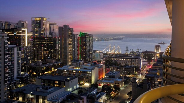 A cityscape at dusk with illuminated buildings and a bridge in the distance.