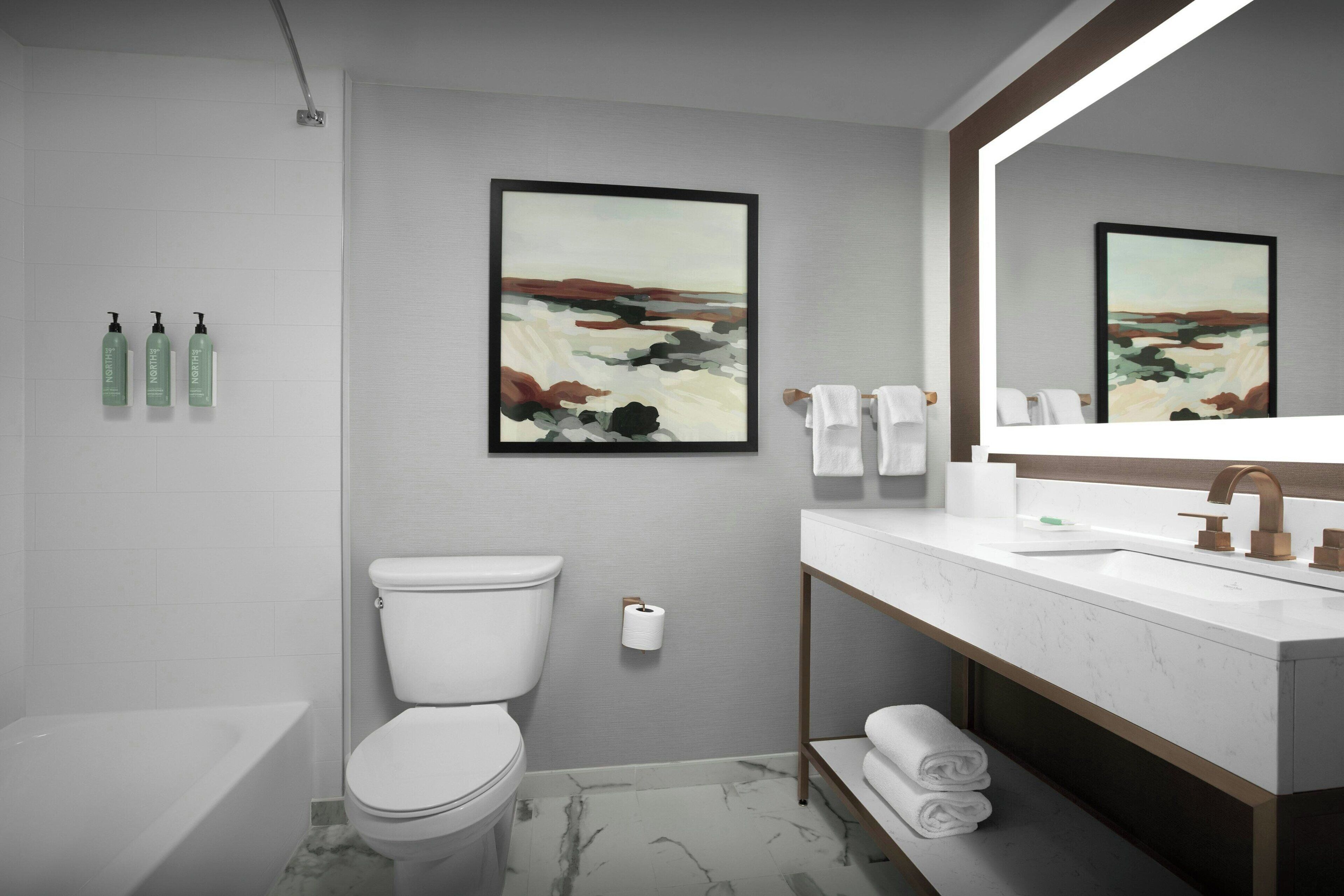 A modern bathroom with a toilet, sink, and bathtub. There are towels and toiletries on the counter.