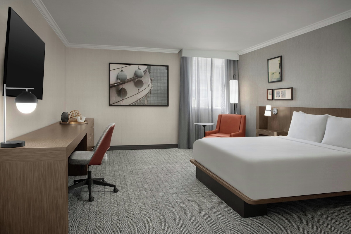 Una habitación de hotel con cama, escritorio, silla y obras de arte en las paredes.
