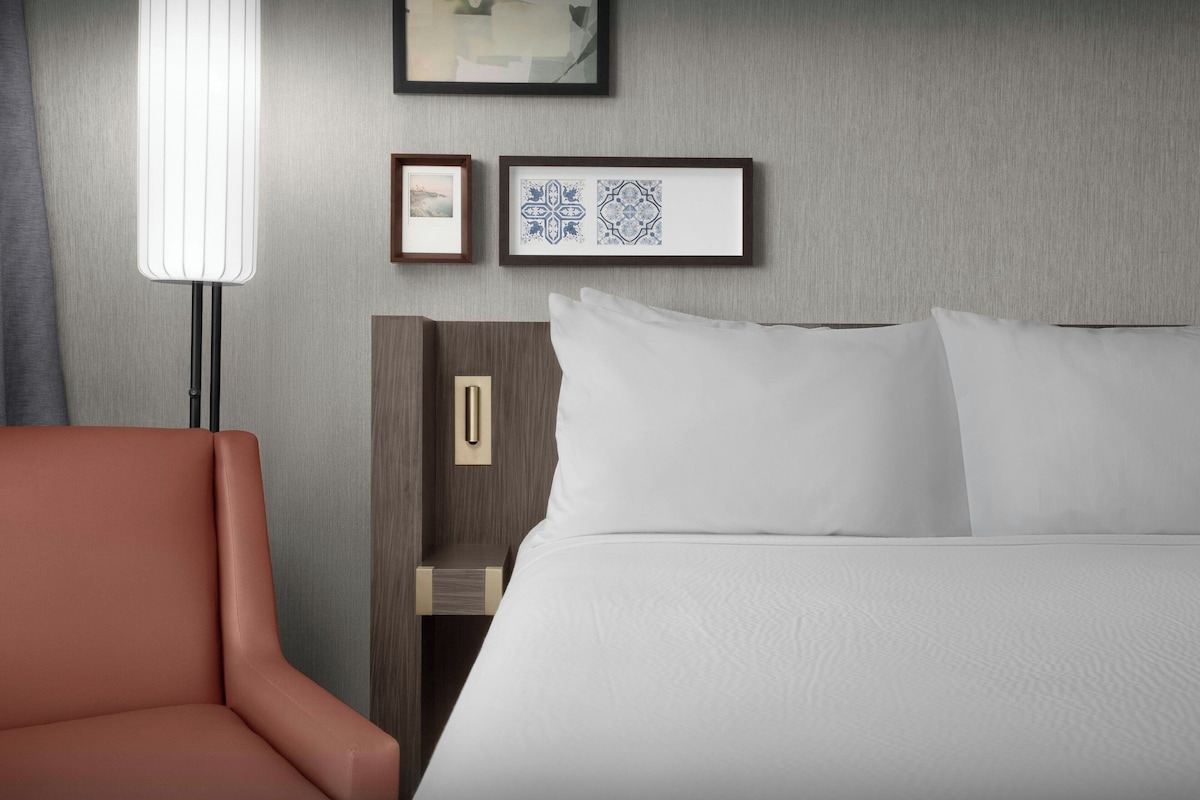 Una habitación de hotel con cama, mesita de noche, lámpara y silla.