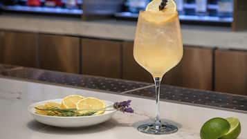 A cocktail glass with a lemon slice garnish, a plate with lemon slices and rosemary, and a lime on a marble countertop.