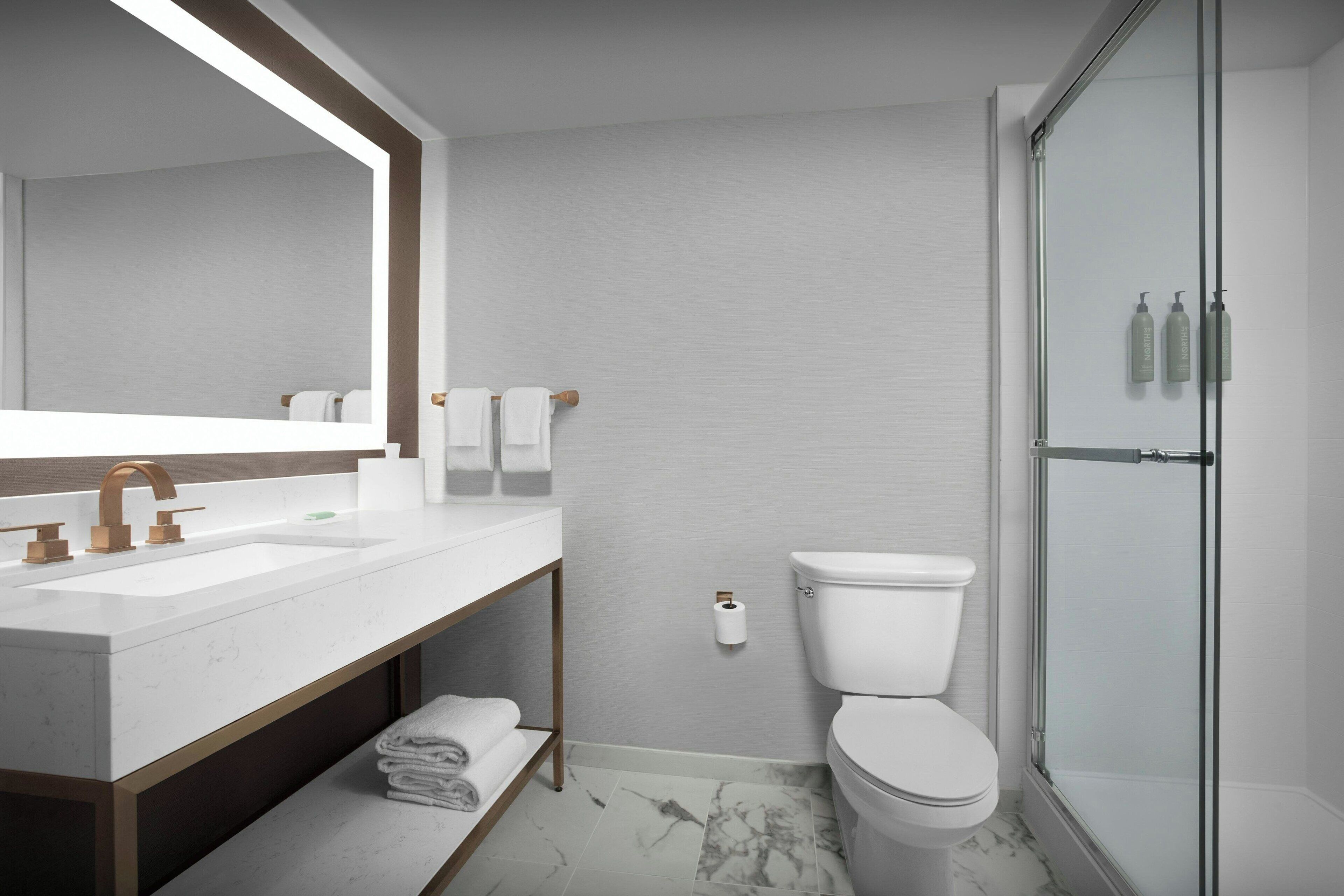 A modern bathroom with a large mirror, dual sinks, a toilet, and a glass-enclosed shower.