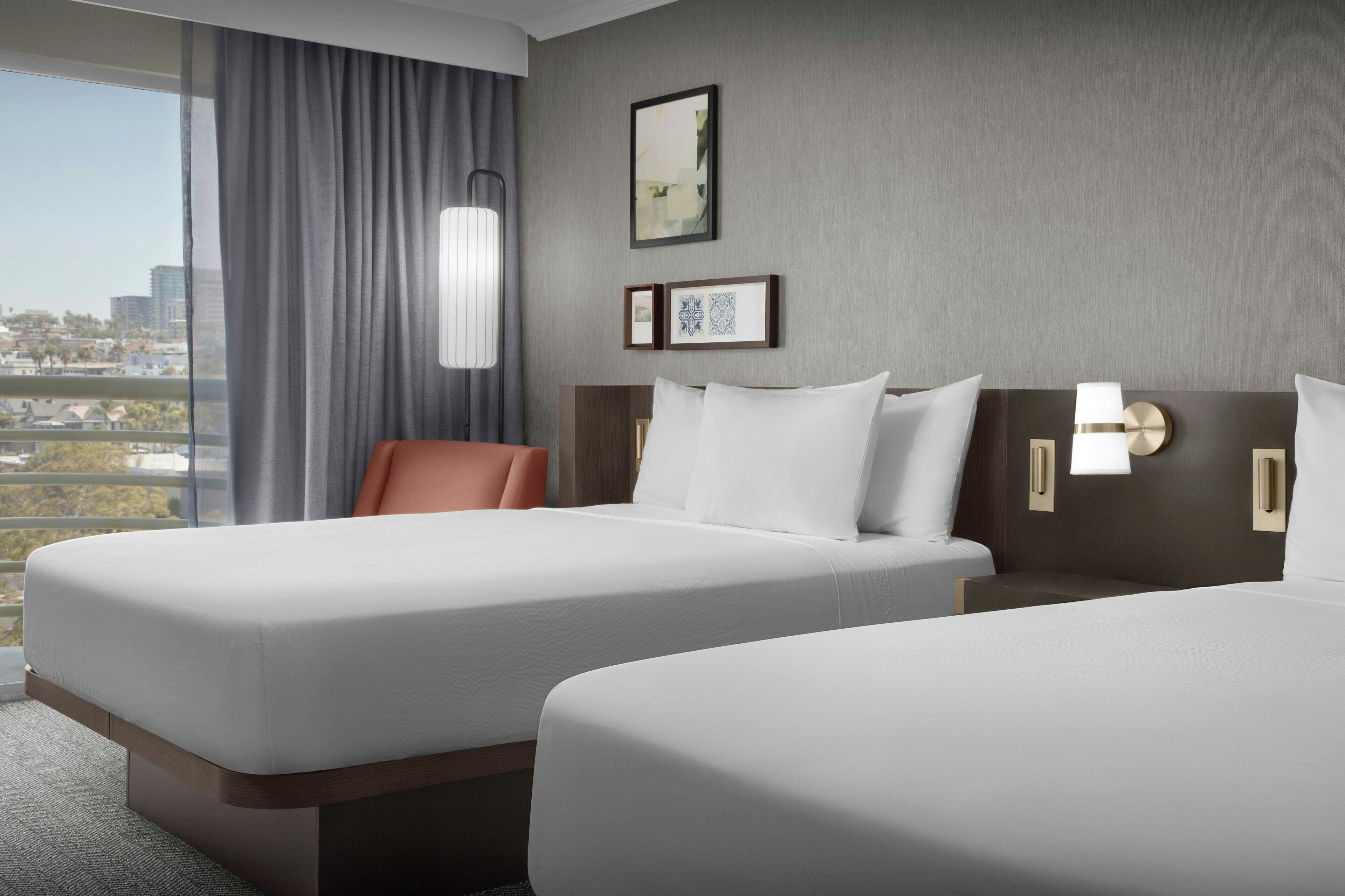 A hotel room with two beds, a view of the city, and a large window with curtains.