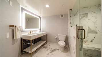 A modern bathroom with a marble floor, a white sink, a toilet, and a glass shower enclosure.