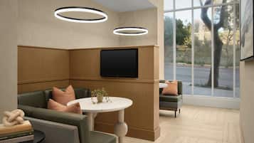A modern waiting area with a flat-screen TV mounted on the wall, a round table with a potted plant, and a seating area with cushioned chairs and sofas.