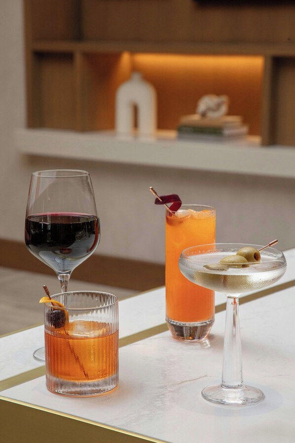 A table with three glasses of different beverages, a white candle, and a decorative item on the shelf behind. - Courtyard by Marriott San Diego Downtown Little Italy (San Diego)