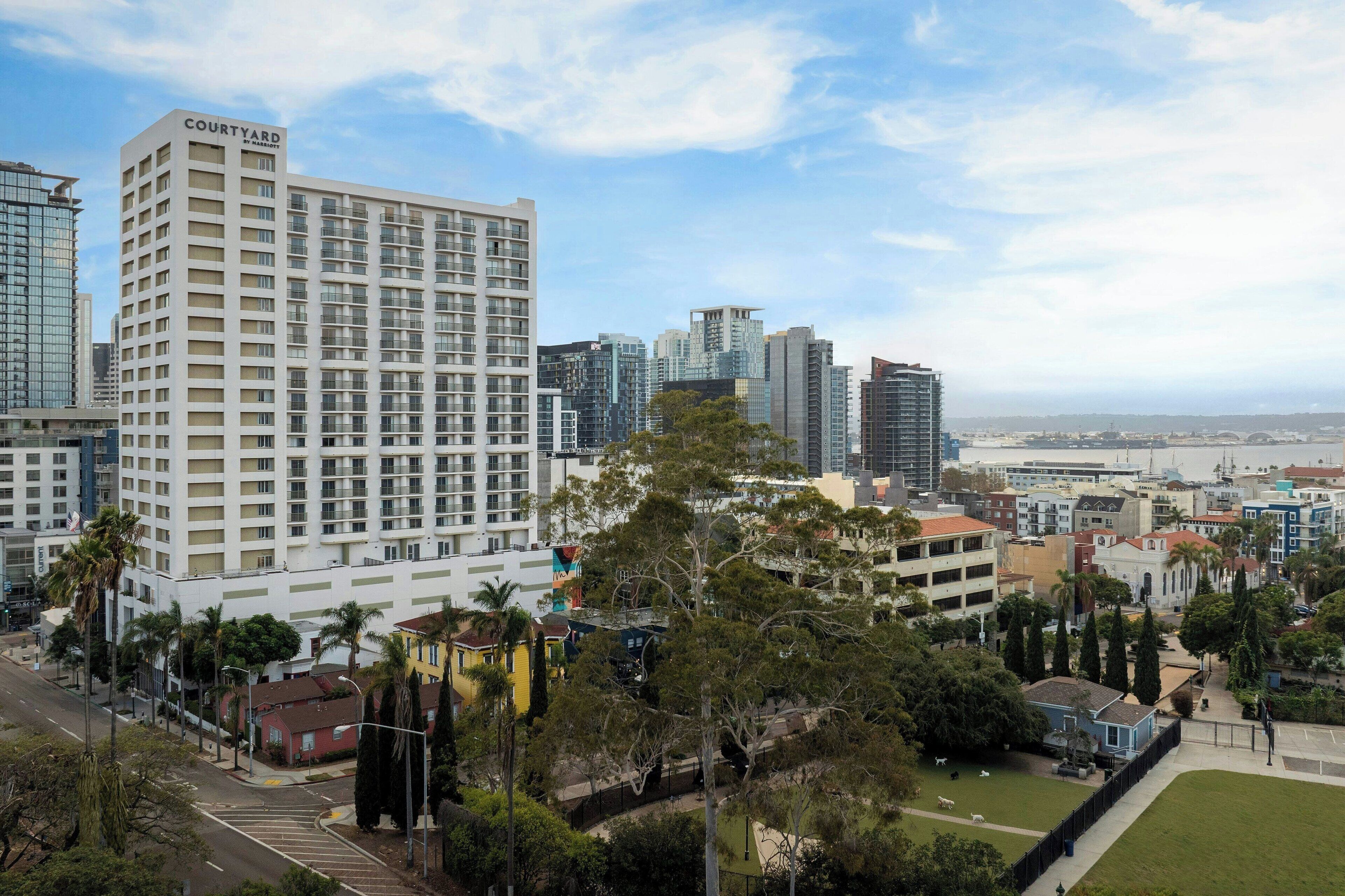 A multi-story hotel with a prominent 'Courtyard' sign, surrounded by other buildings and greenery.