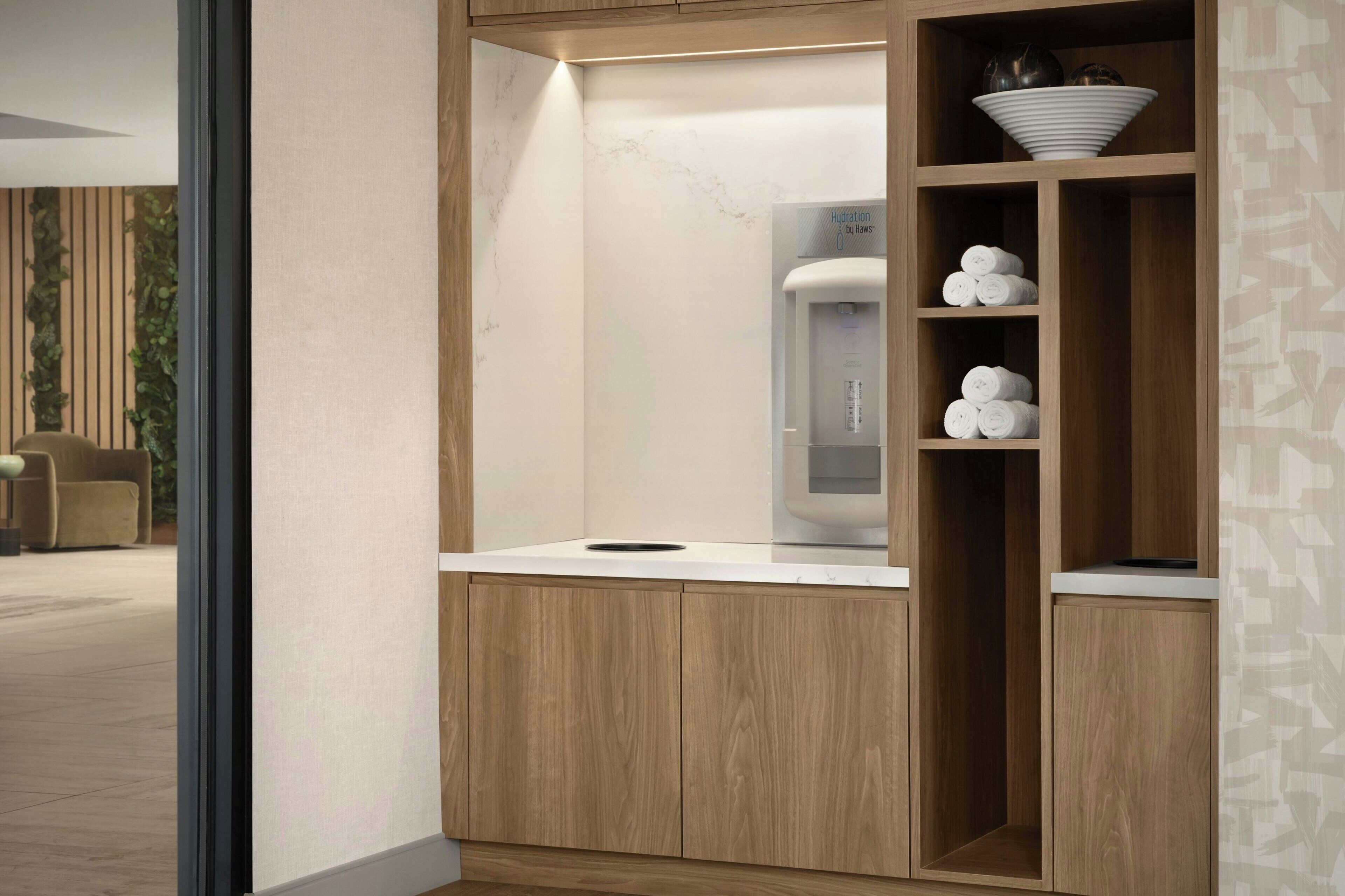 Un baño moderno con tocador de madera, dispensador de agua integrado y toallas dobladas con cuidado.