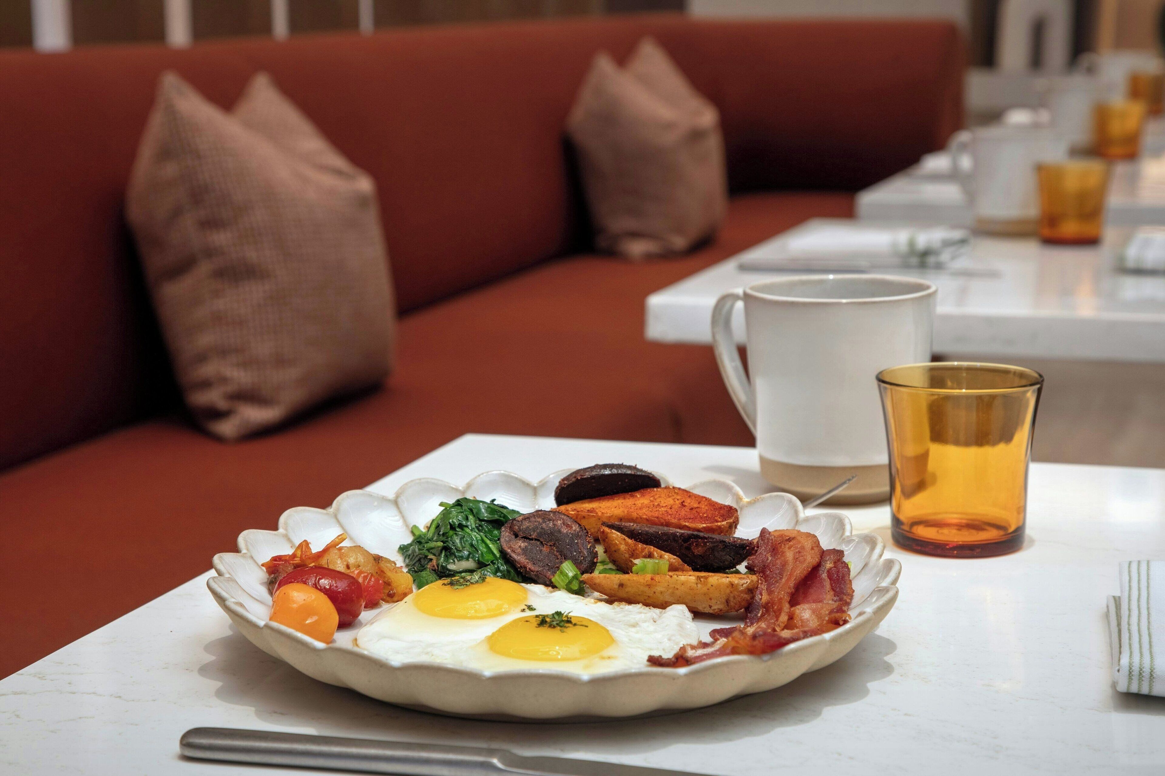 Un plato de desayuno con huevos, tocino, papas y verduras sobre un plato blanco.