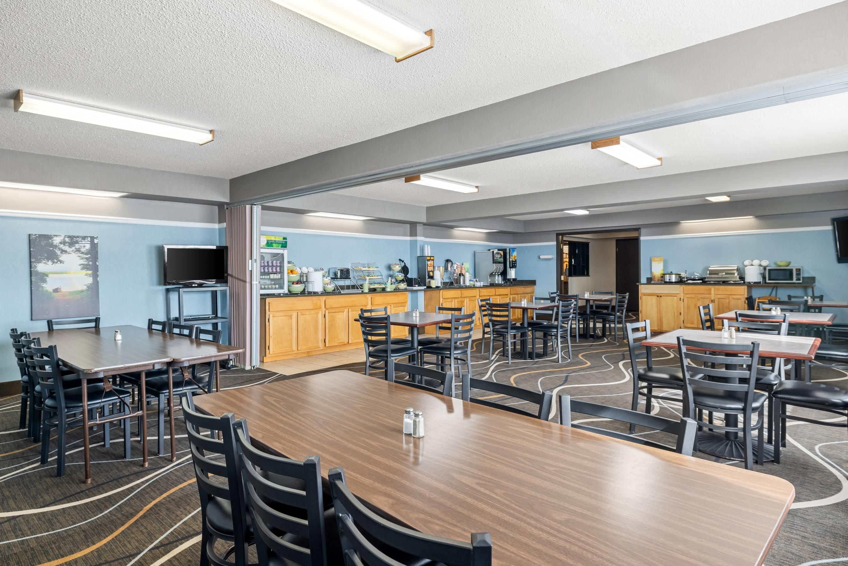 A spacious dining area with multiple tables and chairs, a kitchen area with appliances, and a television mounted on the wall.