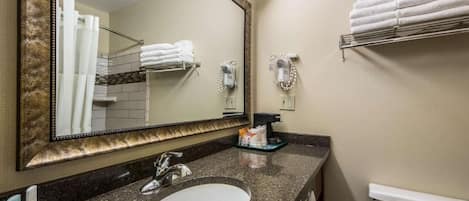Un bany amb un mirall gran, un lavabo, penjalls per tovalloles i un assecador.