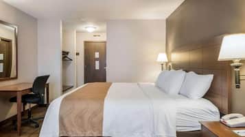 Quarto de hotel com cama, escrivaninha, cadeira e luminária.