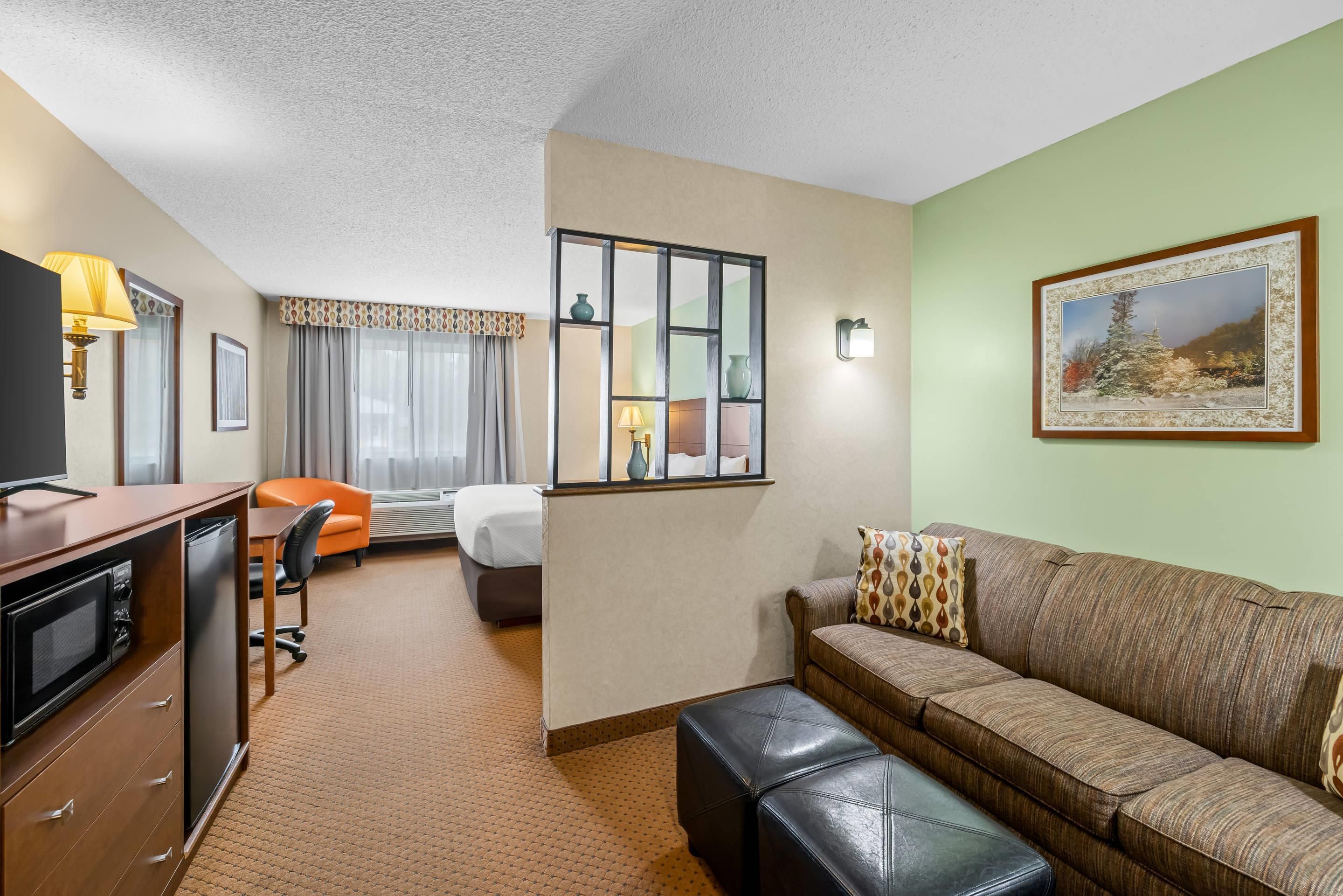 A hotel room with a kitchenette, a sofa, a dining table, a bed, and a large window.