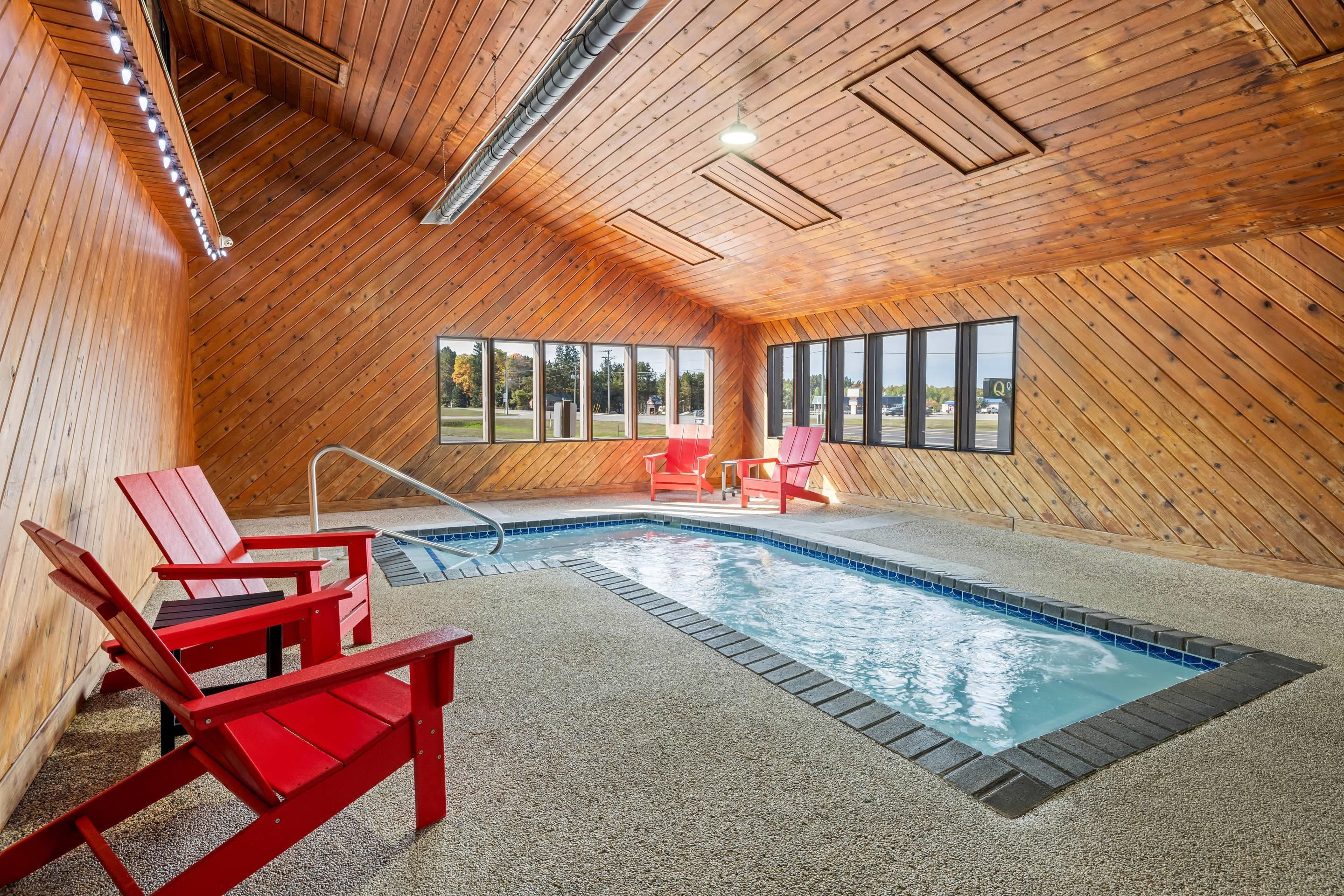 An indoor swimming pool with a wooden interior, red chairs, and a view of the outside.