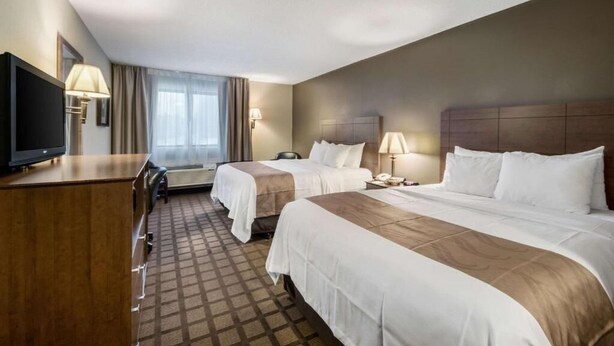 Ein Hotelzimmer mit zwei Betten, einem Schreibtisch mit Fernseher und einem Fenster mit Vorhängen.
