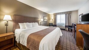 Ein Hotelzimmer mit einem großen Bett, Nachttischen, einem Schreibtisch, einem Sessel, einem Fernseher und einem Fenster mit Vorhängen.