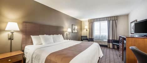 A hotel room with a large bed, bedside tables, a desk, a chair, a television, and a window with curtains.
