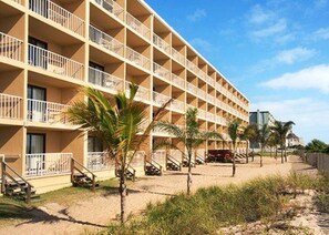 A multi-story hotel with balconies and a sandy ground floor.